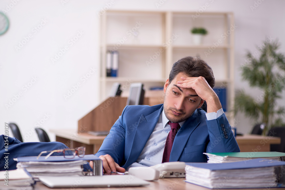 Young male employee unhappy with excessive work in the office Young male employee unhappy with excessive work in the office