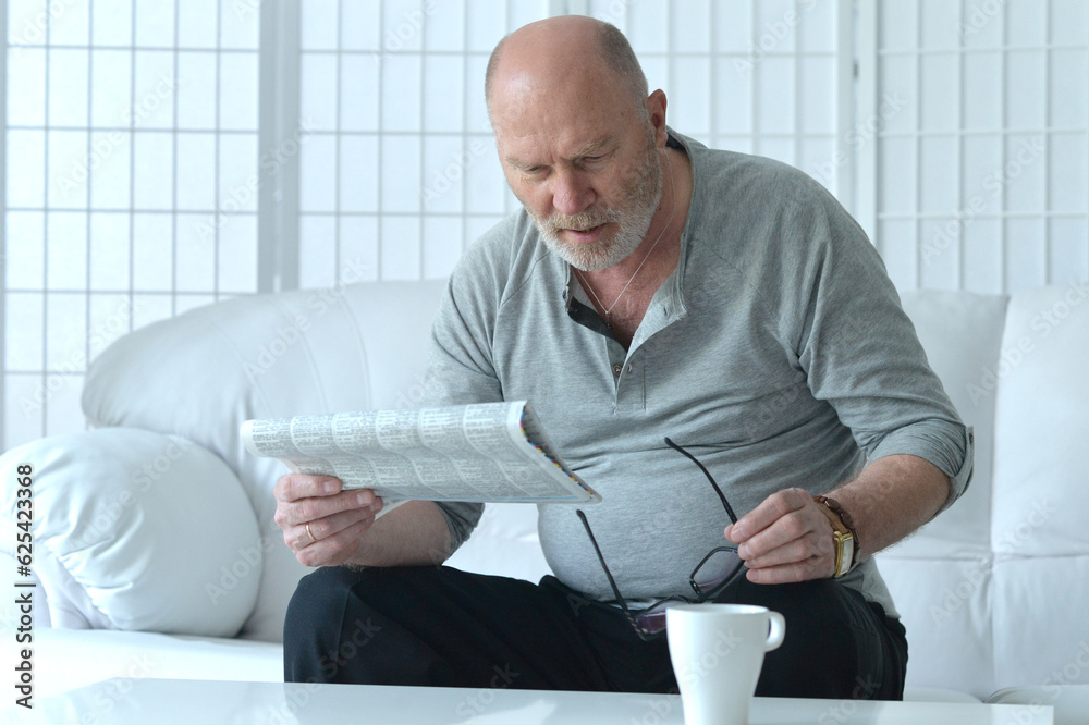 Senior old man reading newspaper at home