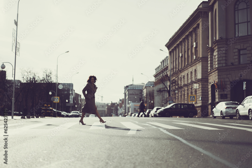 Young woman walks on the crossroad through the autumn city