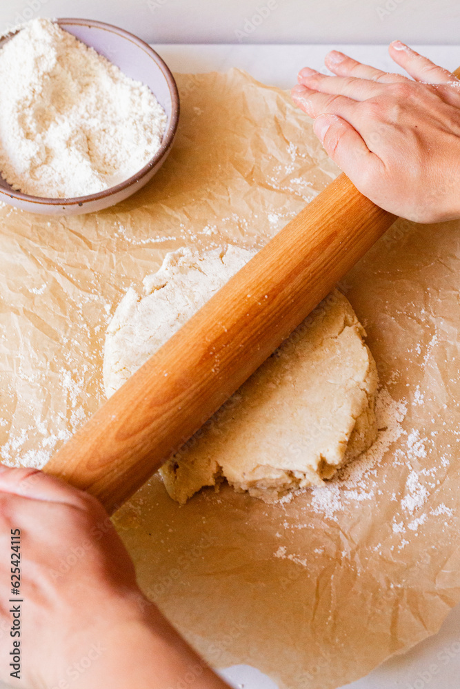 Hands roll out pie dough with a wooden rolling pin Hands roll out pie dough with a wooden rolling pin