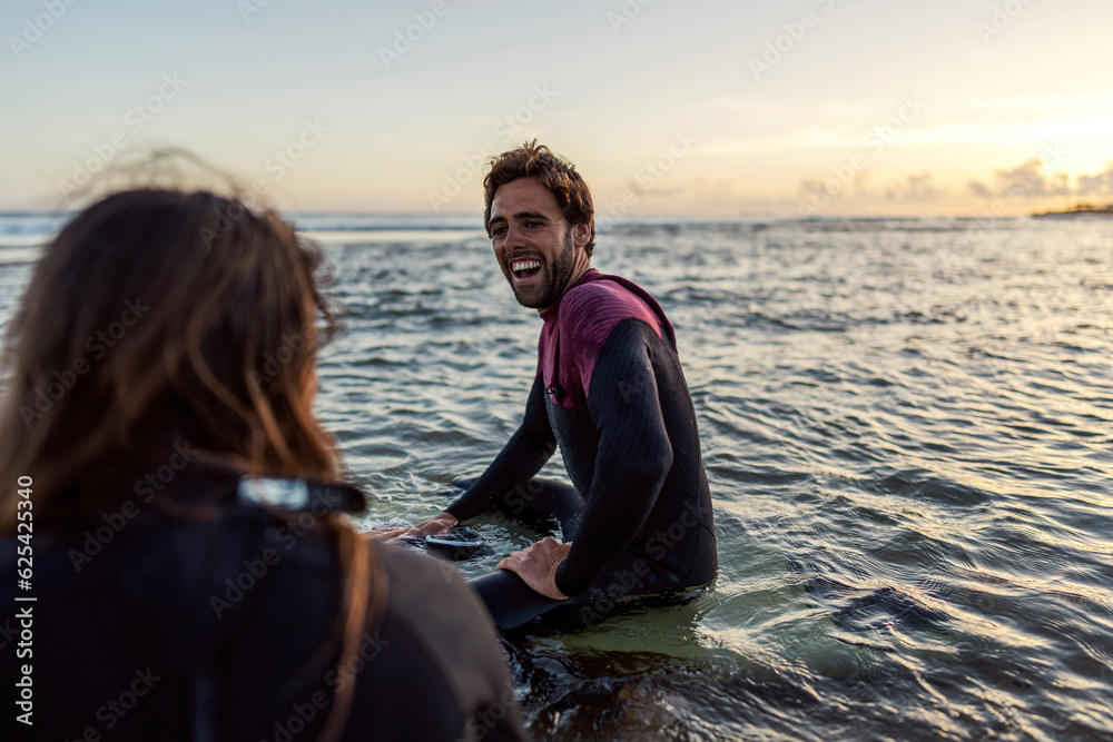 Fototapeta premium Happy surfers laughing at each other while sitting on the surfboards in water.