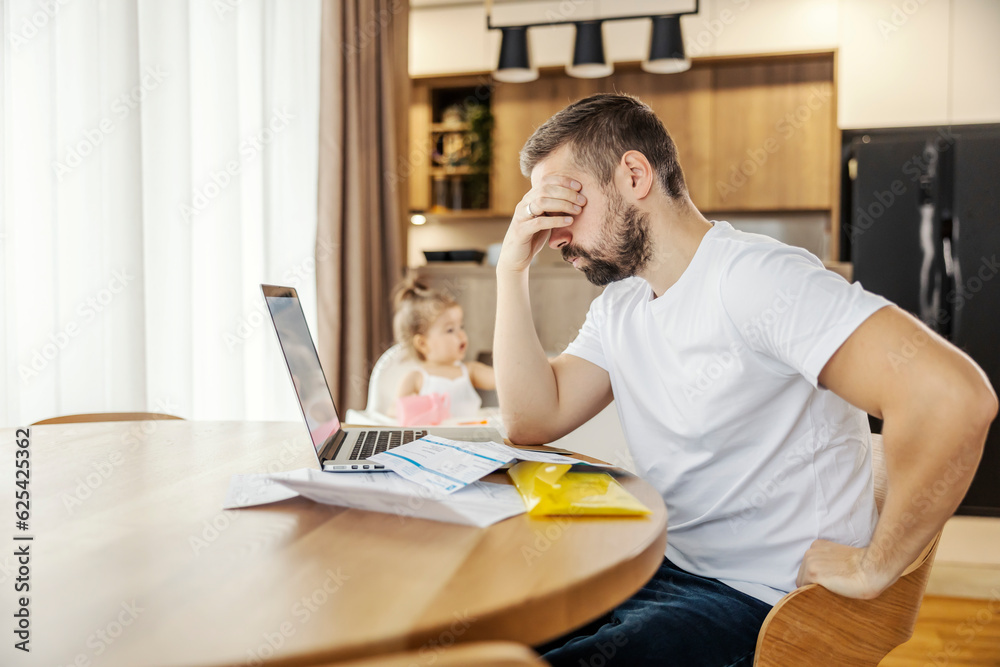 A depressed man is having headache from paying the bills form home while his daughter is playing careless. A depressed man is having headache from paying the bills form home while his daughter is playing careless.