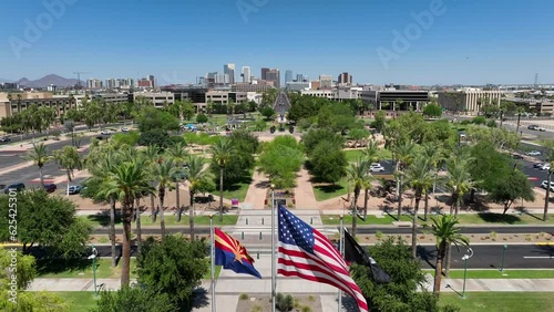 American flag, Arizona state flag, and POW MIA flags waving in on capitol grounds. Aerial rising shot revealing Phoenix, Arizona skyline. photo