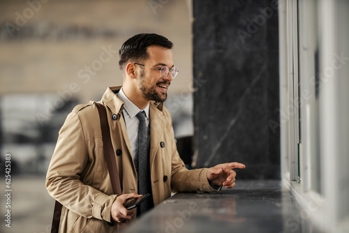 фотографія A happy smart casual man is talking to counter clerk and buying train ticket