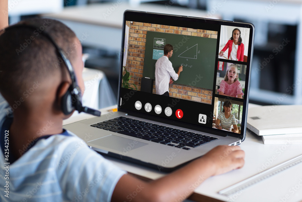 African american boy in headphones listening to teacher teaching over video call on laptop
