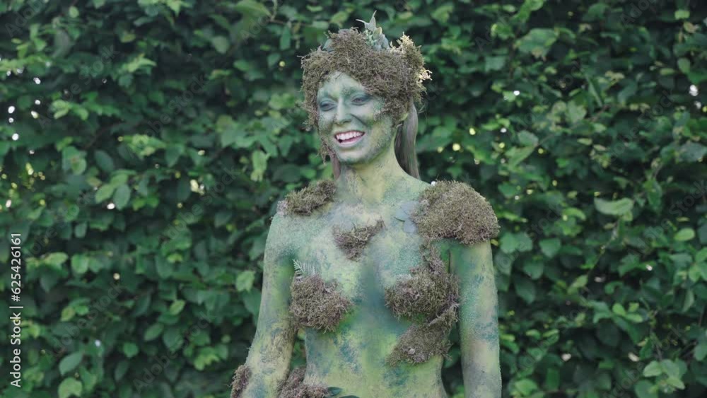 Medium shot of a female model laughing wearing green bodypaint watching forwards in a forest, in the style of nature-inspired forms Medium shot of a female model laughing wearing green bodypaint watching forwards in a forest, in the style of nature-inspired forms