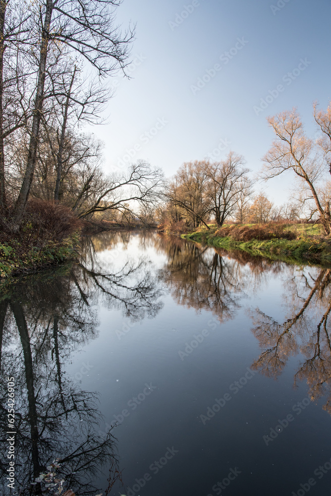 River with trees around mirroring on water ground during autumn day with clear sky River with trees around mirroring on water ground during autumn day with clear sky