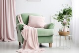 A comfortable bedroom interior features a cozy armchair with a pink color, adorned with a white pillow. The green mattress is covered with a blanket.