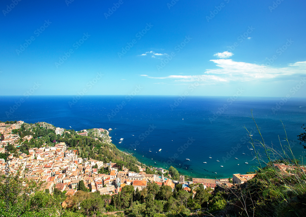 Photograph of the coast of Taormina in Sicily, houses, boats and trees.