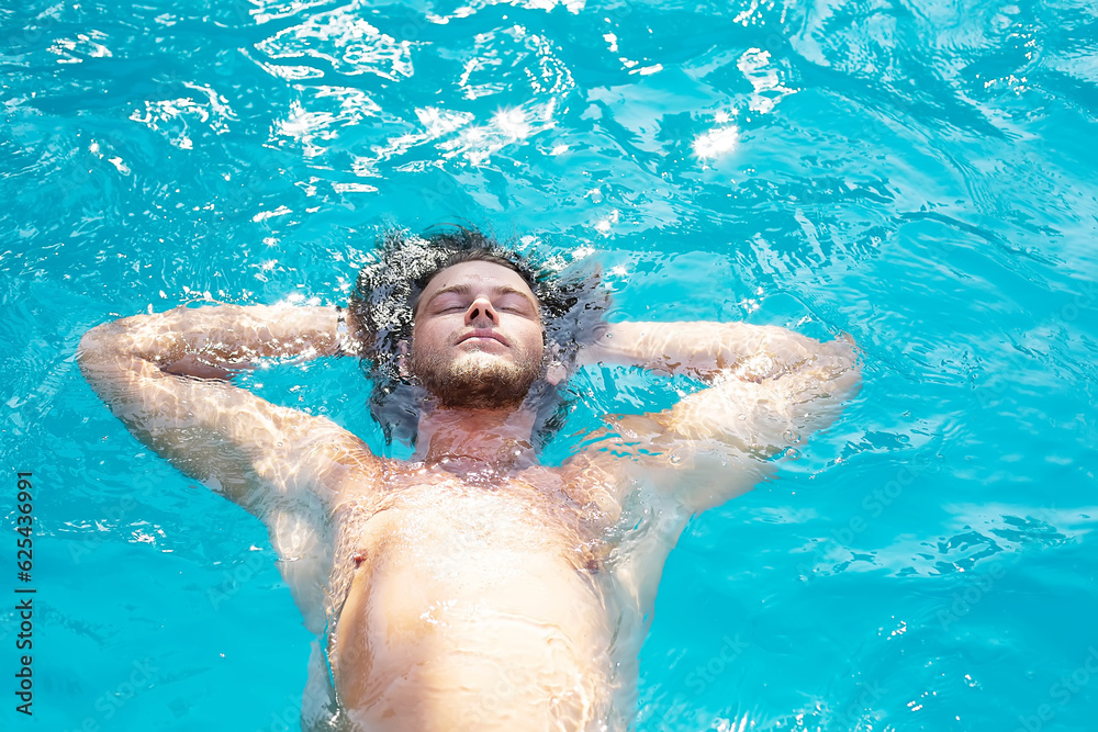A YOUNG GUY IS LYING WITH HIS BACK ON THE WATER IN THE POOL ENJOYING THE WARMTH AND RESTING