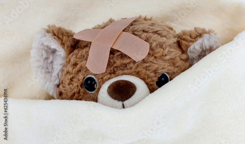 Fotografering Sick teddy bear toy with patch in on head lying in bed