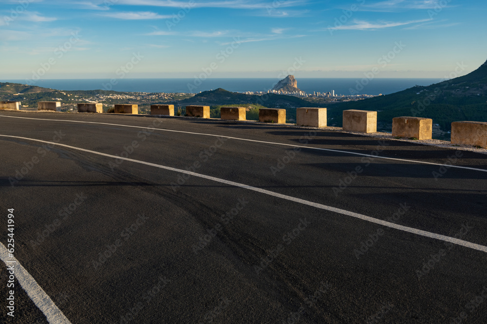 Naklejka premium Empty winding mountain road, Calpe village at background, Alicante, Costa Blanca, Spain