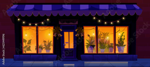 Flower shop facade in night city street. Vector cartoon illustration of urban floral boutique, gift storefront with illuminated windows and garlands, striped tent above door, flowerpots on shelf