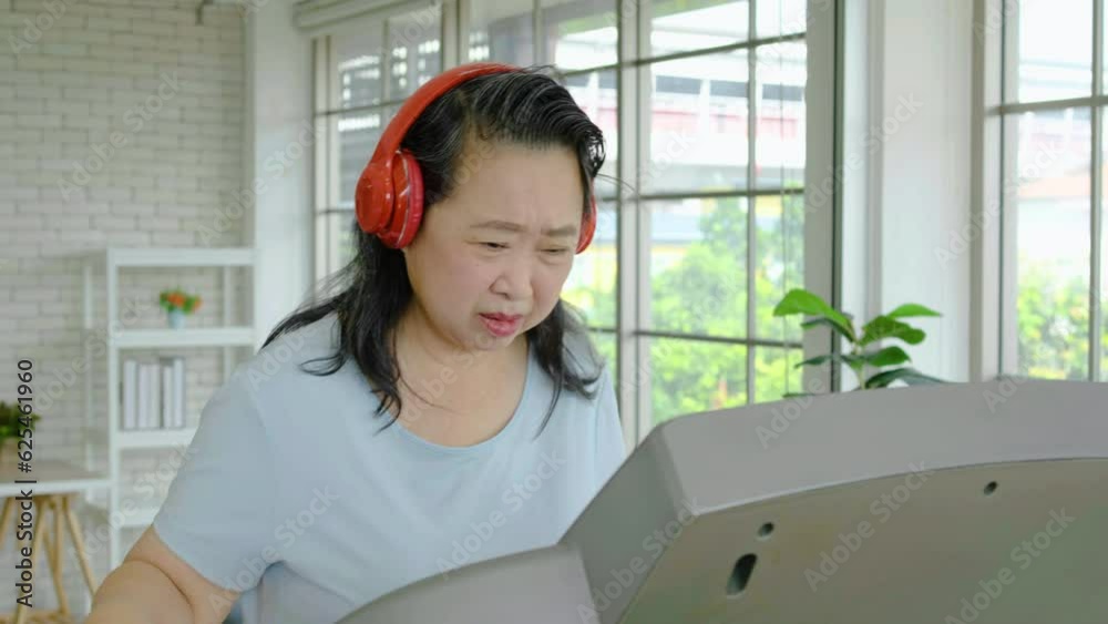 Senior asian woman grandmother wearing headphones making video call with smart phone to friends or family to show her achievements and results while workout in home Senior asian woman grandmother wearing headphones making video call with smart phone to friends or family to show her achievements and results while workout in home