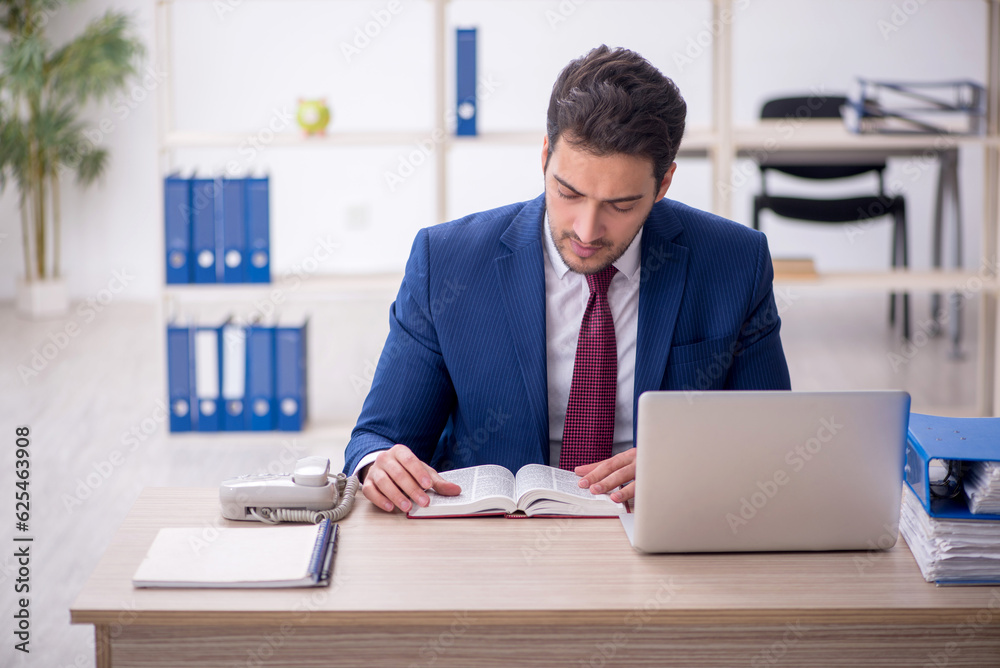Young male employee reading book at workplace Young male employee reading book at workplace