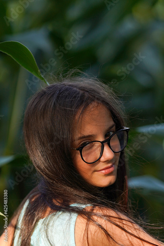 Pretty brunette with glasses looking with her head turned back, green plant background.