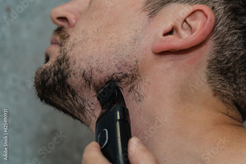 Handsome man shaving his beard by electric razor