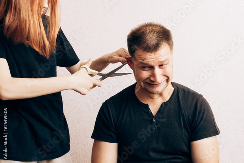 Red-haired girl cuts the guy's hair with scissors