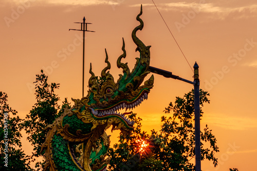 The background of the setting sun around the mountain range and there is an old church at Chiang Rai Province of Thailand or Wat Huai Khian, with beautiful old sculptures. © bangprik