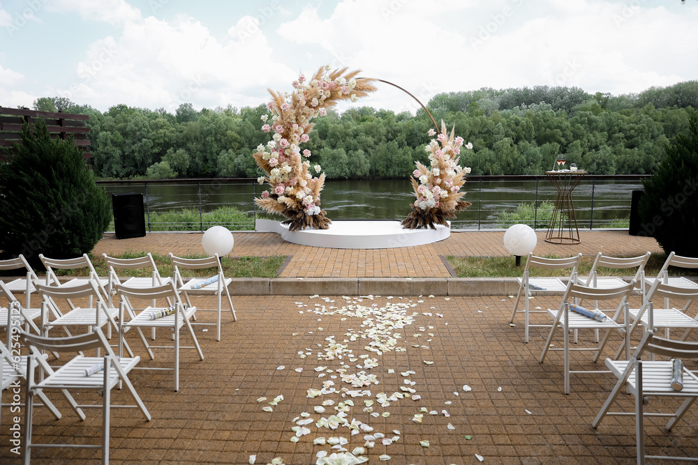 A beautiful wedding arch, decorated with flowers and greenery, near a lake or river in the open air. Decorations for an outdoor wedding ceremony. High quality photo