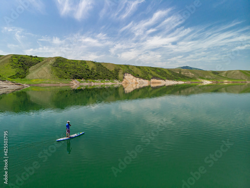 A bearded man swims on a SUP board on a lake among the rocks. Stand Up Paddling. Mountain lake with azure water