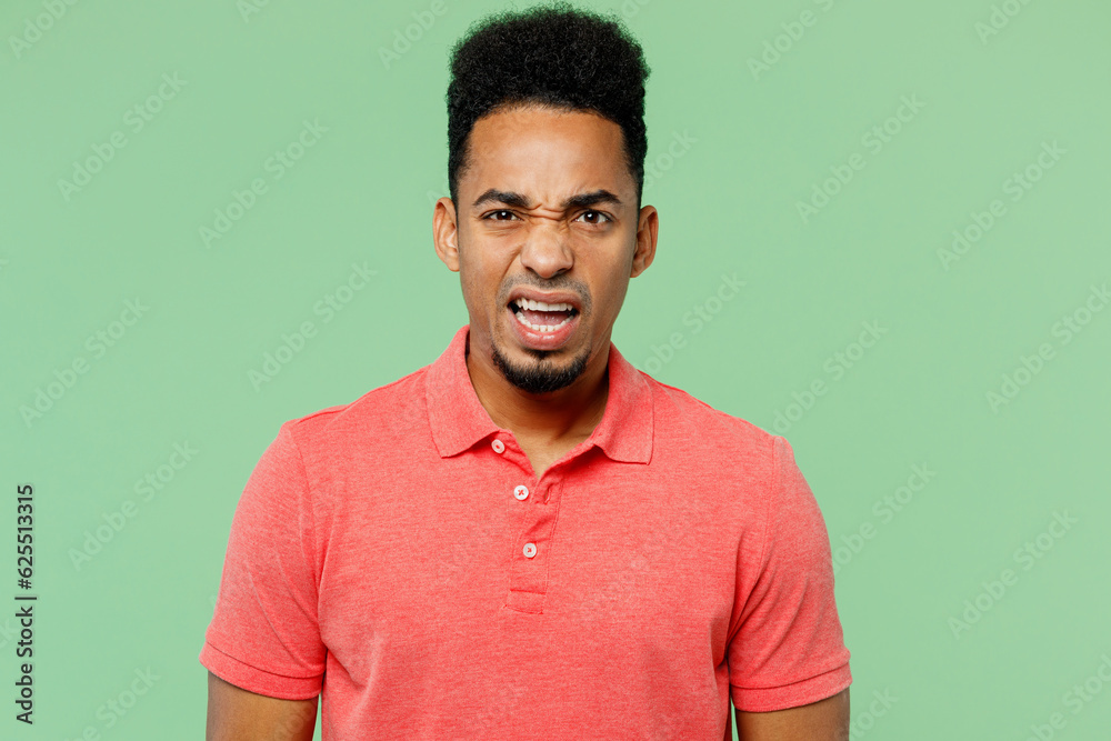 Young dissatisfied displeased disappointed sad man of African American ethnicity wears pink t-shirt looking camera isolated on plain pastel light green background studio portrait. Lifestyle concept. Young dissatisfied displeased disappointed sad man of African American ethnicity wears pink t-shirt looking camera isolated on plain pastel light green background studio portrait. Lifestyle concept.