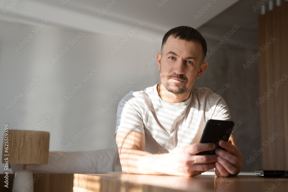 man  with mobile phone  reads messages or news sitting at the table at home. concept without stress. mental health. work from vacation home.