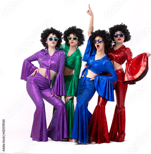 A group of girls in colorful flared suits and afro wigs pose against a white background. Disco style from the eighties or seventies.
