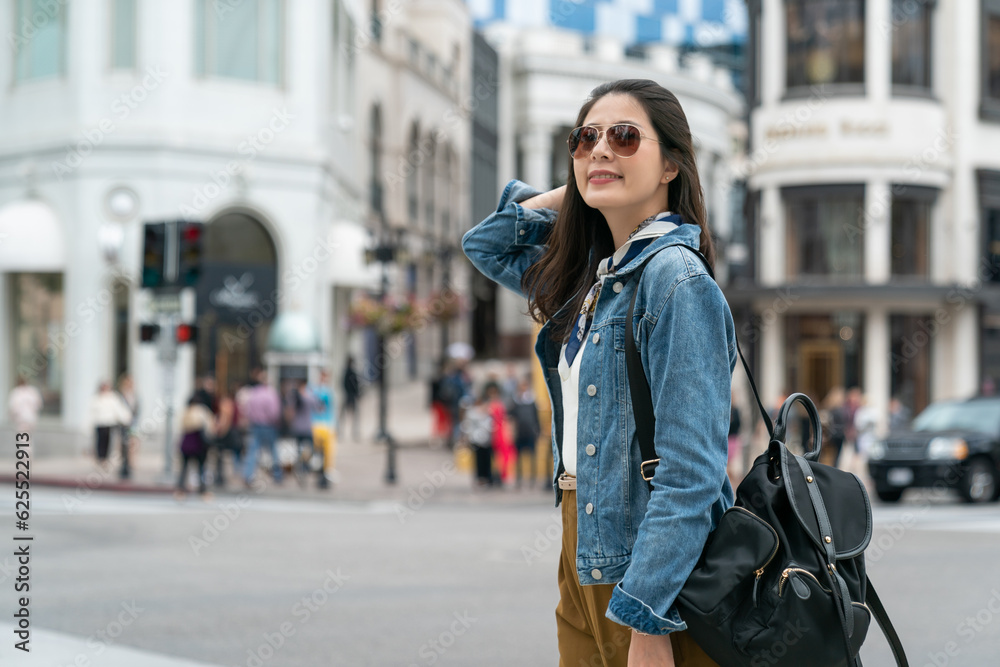 Fototapeta premium chinese woman standing on street is combing hair with hand and looking back with a charming smile.