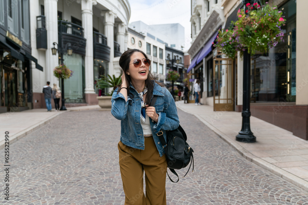 Fototapeta premium Cheerful asian woman in a jean jacket smiles sincerely outdoors. Happy lady laughs and walks in great mood outside.