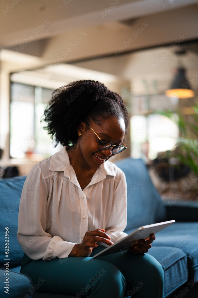 Beautiful African businesswoman sitting on sofa in office. Young woman using digital tablet. Beautiful African businesswoman sitting on sofa in office. Young woman using digital tablet.