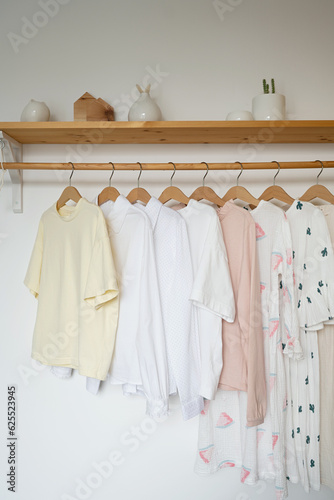 Child clothes on hangers in a room with white walls and wooden shelf in the interior