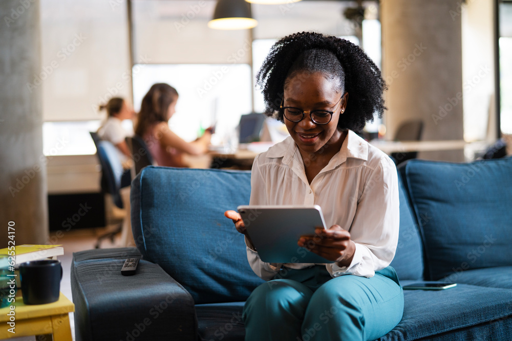 Beautiful African businesswoman sitting on sofa in office. Young woman using digital tablet. Beautiful African businesswoman sitting on sofa in office. Young woman using digital tablet.