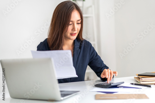 Smiling asian woman using calculator and calculate bills on laptop, paying bill, credit card, finance, tax, vat, credit card, payment, tax refund, budget, debt, money.financial and accounting concept