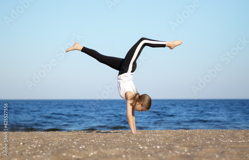 A young sporty girl does somersaults with raised legs against the background of the sea. Selective focus. Blurred background