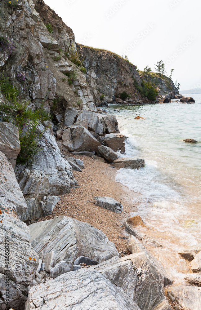 Baikal Lake in summer. Beautiful sandy beach of Olkhon Island in a small bay with smooth large stones. Summer hiking, active recreation on the shores of the Small Sea. Natural background