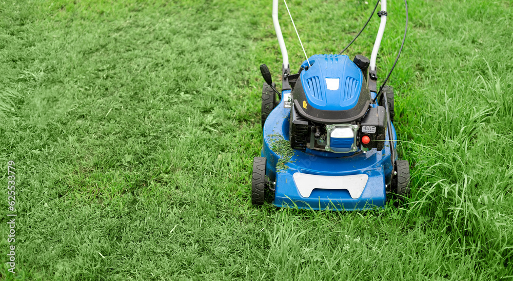 Lawn mower cutting grass. Small grass cuttings fly out of lawnmower. Grass clippings get spewed out of a mower pushed around by landscaper. CloseUp. Gardener working with mower machine. Mowing lawns Lawn mower cutting grass. Small grass cuttings fly out of lawnmower. Grass clippings get spewed out of a mower pushed around by landscaper. CloseUp. Gardener working with mower machine. Mowing lawns