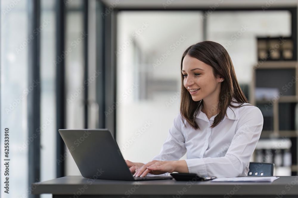 Young happy professional business woman working on laptop in office sitting at desk, business female portrait at workplace Young happy professional business woman working on laptop in office sitting at desk, business female portrait at workplace
