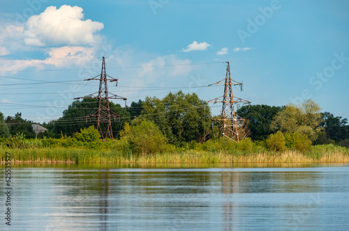 Old rusty pylons of a high-voltage power line on the banks of a river or lake on a summer day