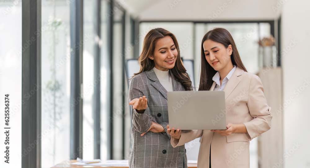 Two happy professional coworkers discussing plan at work. explaining Asian colleague financial project on laptop in office Two happy professional coworkers discussing plan at work. explaining Asian colleague financial project on laptop in office