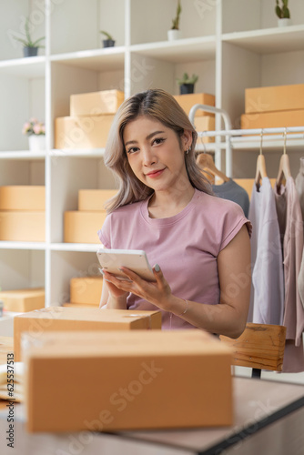 Asian woman entrepreneur beautiful sell clothes online with laptop and product order calculator in office. Online store parcels © Natee Meepian