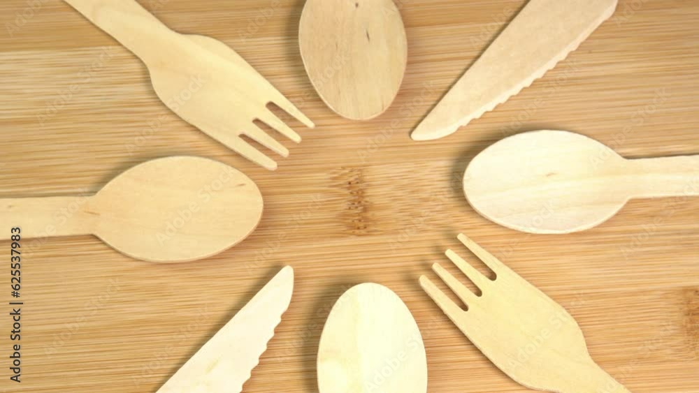 Wooden eco-friendly disposable tableware rotate. Pile of wooden spoons, forks and knives on cutting board surface. Disposable ecological tableware for kitchen and restaurant