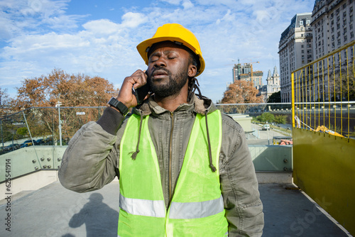 young black man construction worker with closed eyes is upset and tired talking on the phone