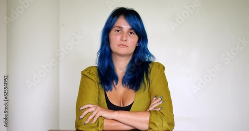 Young woman with bright blue hair stares directly into camera with intense and commanding gaze. Her expression is attentive, incredulous, and stern, showcasing her self-power and confidence photo