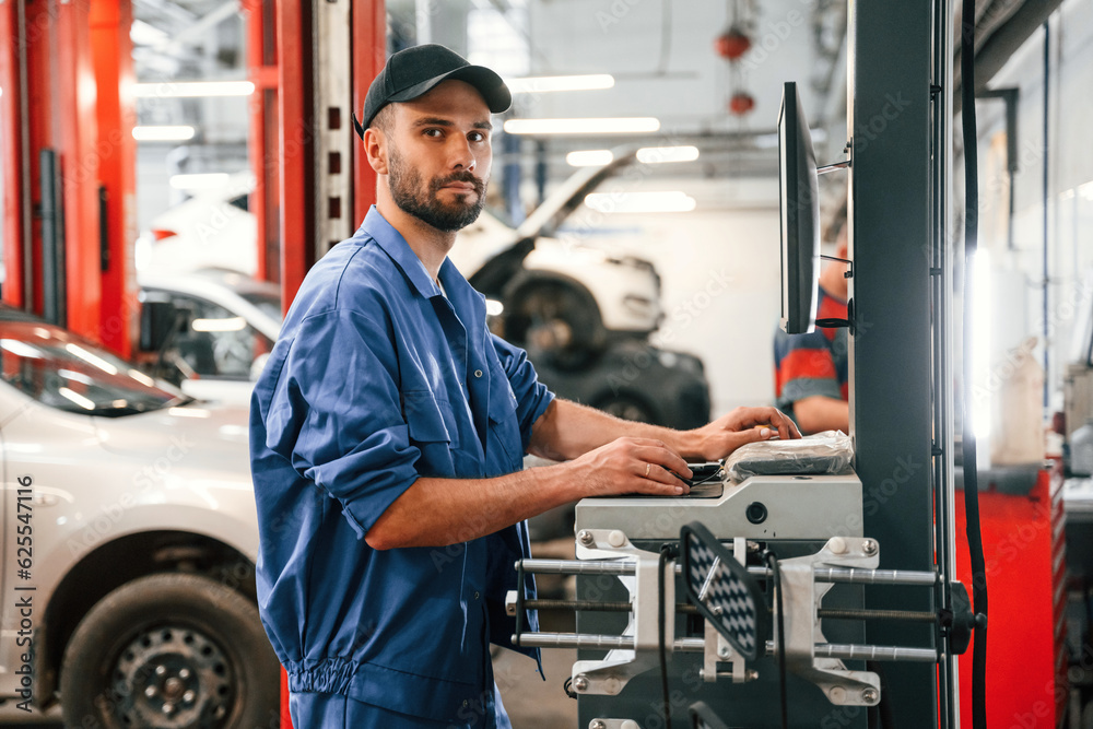 Side view, using computer. Auto mechanic working in garage. Repair service Side view, using computer. Auto mechanic working in garage. Repair service