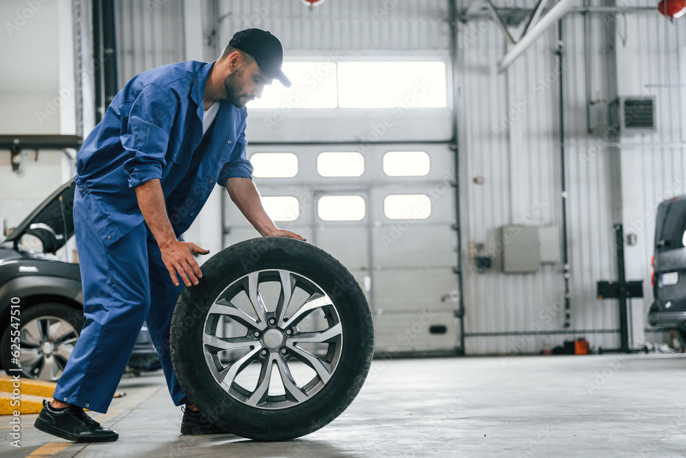 New tire, moving it. Auto mechanic working in garage. Repair service New tire, moving it. Auto mechanic working in garage. Repair service