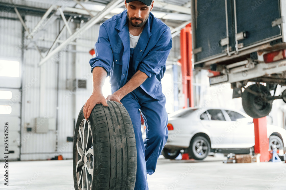 Walking forward with new tire. Auto mechanic working in garage. Repair service Walking forward with new tire. Auto mechanic working in garage. Repair service