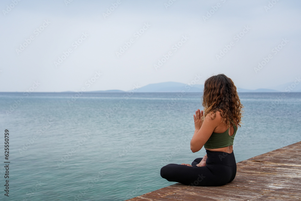 Woman practicing yoga by the sea on a deck - Namaste / namaskar / Anjali mudra ve Padmasana Lotus