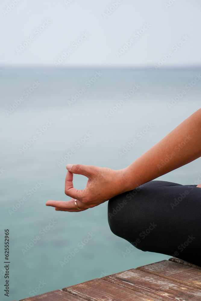 Woman practicing yoga by the sea on a deck - Padmasana / Lotus pose / meditation sitting - chin mudra