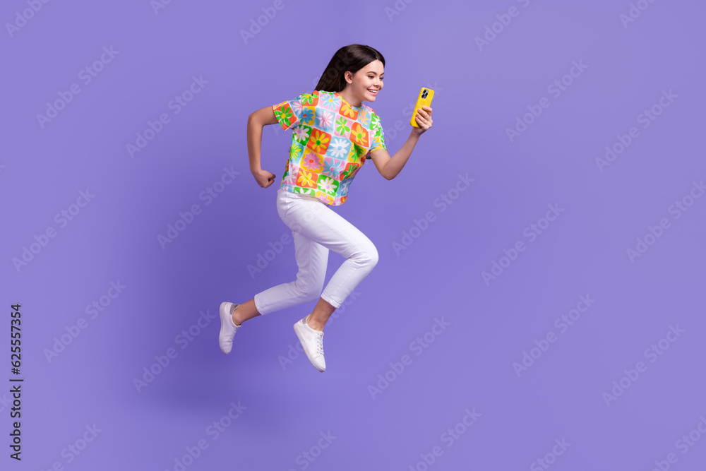 Full length photo of funny positive girl dressed flower print t-shirt running with smartphone in hand isolated on violet color background